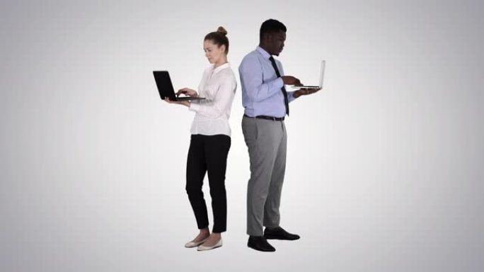 夫妇背靠背站立，在渐变背景下在笔记本电脑上工作