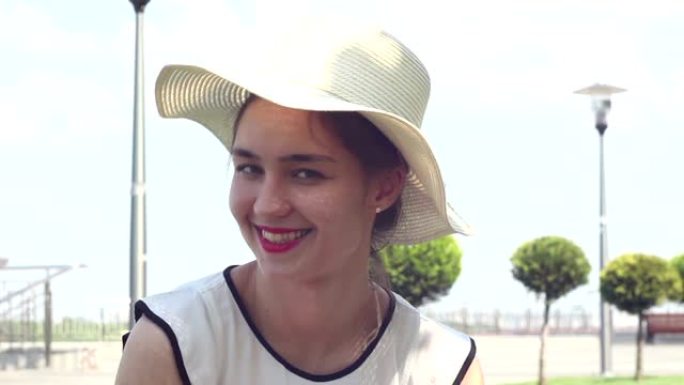 特写肖像一个戴着白帽子的美丽年轻女孩看着镜头微笑。一个戴着白帽子的年轻迷人女孩，将目光投向天空，斜视