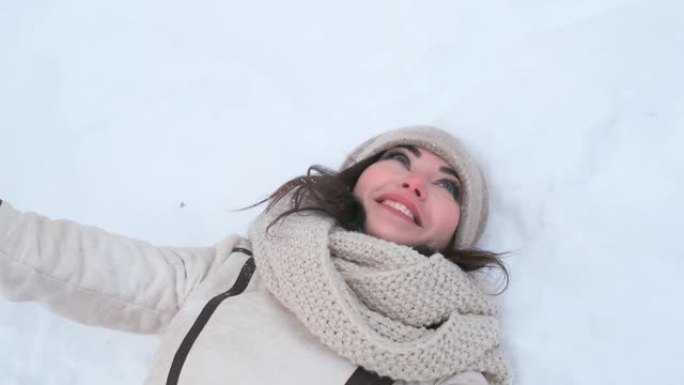 冬天森林里迷人的年轻蓝眼睛女人躺在雪浪上，她的手捕捉雪，欢欣鼓舞。特写。慢动作