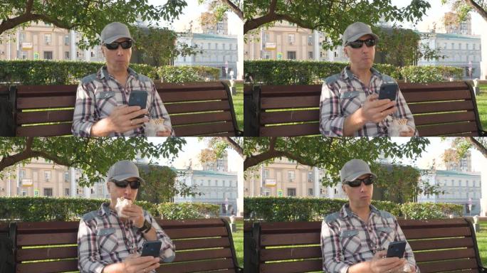 戴墨镜的白人男子坐在公园的长凳上吃智能手机的点击