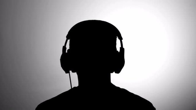 男士黑色剪影对着灰色墙壁戴着耳机听音乐