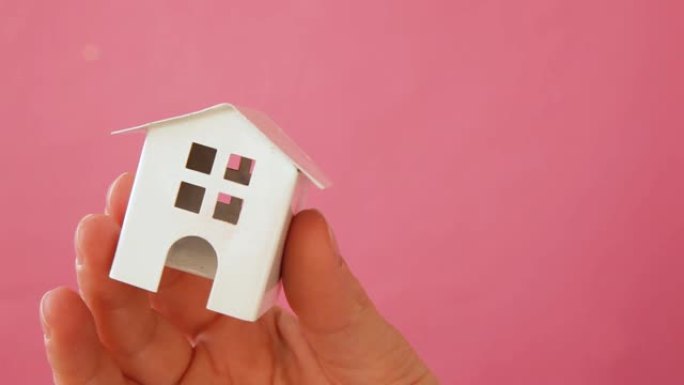 简单设计女性手握微型白色玩具屋孤立在粉色粉彩彩色时尚背景