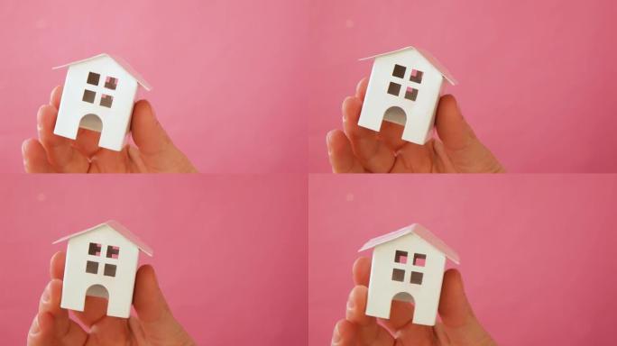 简单设计女性手握微型白色玩具屋孤立在粉色粉彩彩色时尚背景