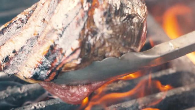 局长用抹刀把肉放在烤架上。火在燃烧，热多汁的油牛排烹饪关闭慢动作。烧烤，美味牛排