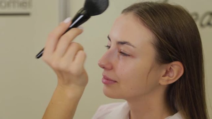 专业化妆师正在用刷子将粉末涂在客户的脸上