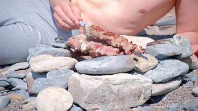 男子正在篝火上煮沙什利克，旋转串躺在石头上，食物特写。