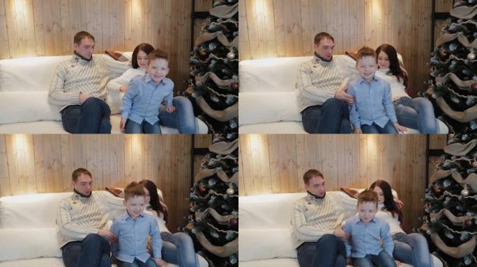 圣诞节之夜，美丽幸福的三口之家在沙发上微笑着在圣诞树旁交谈