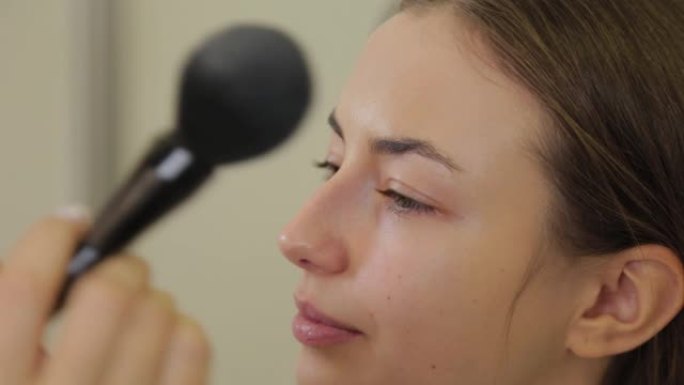 专业化妆师正在用刷子将粉末涂在客户的脸上
