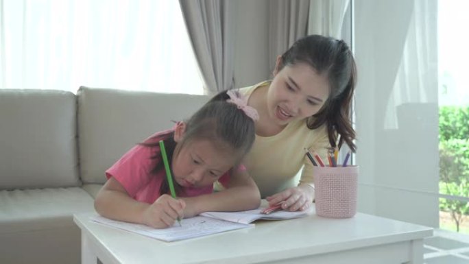 亚洲妈妈和女儿在家里客厅的桌子上用彩色铅笔一起画画。父母身份或爱和结合的表达概念。
