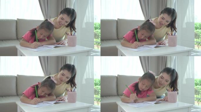 亚洲妈妈和女儿在家里客厅的桌子上用彩色铅笔一起画画。父母身份或爱和结合的表达概念。