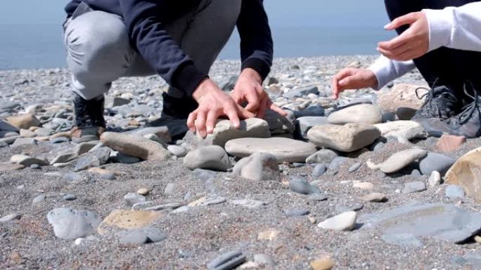 男人和女人正在海边建造一块石头的火盆，近距离的双手。