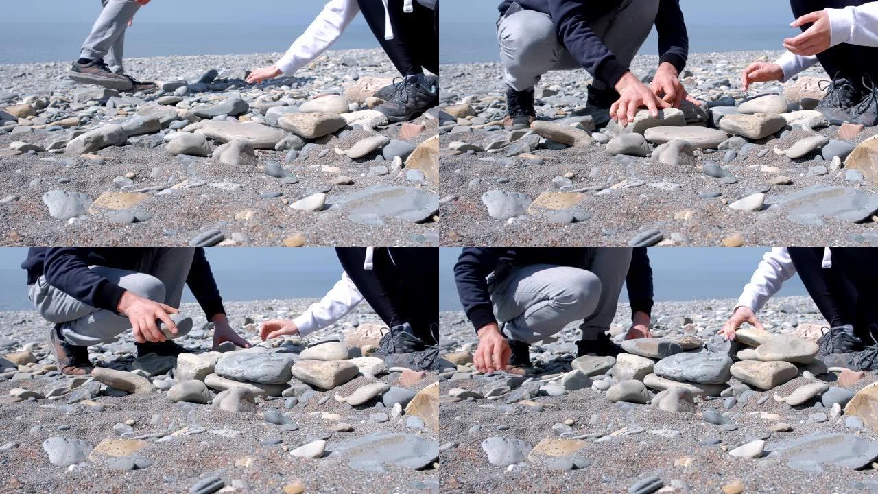 男人和女人正在海边建造一块石头的火盆，近距离的双手。