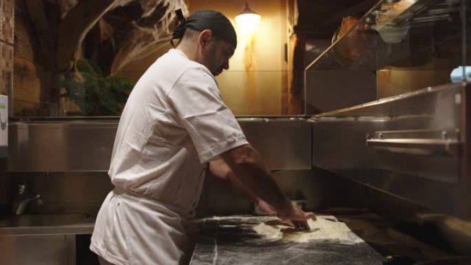 穿着白色围裙和厨师帽的男人用手形成披萨面团