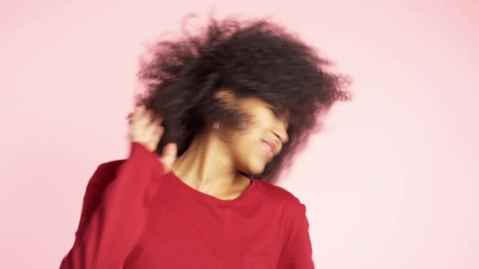 美丽的非洲裔美国女人，有着非洲的头发，在粉色背景下的工作室里微笑和跳舞。4k