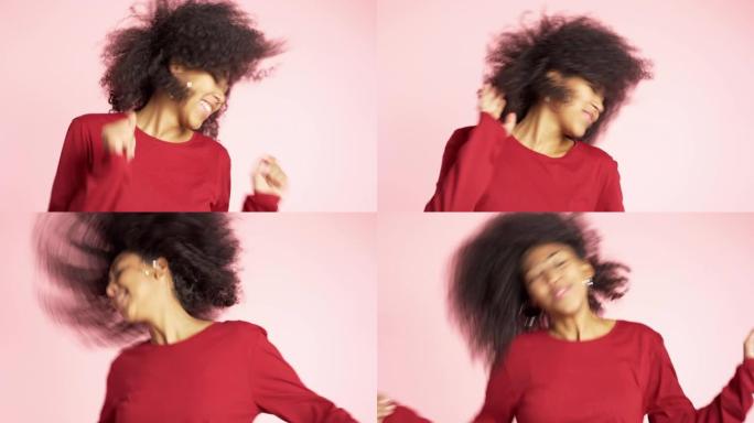 美丽的非洲裔美国女人，有着非洲的头发，在粉色背景下的工作室里微笑和跳舞。4k