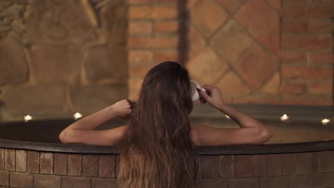 一个年轻女子在温泉里喝香茶时洗热水澡的特写镜头。水疗和健康。孤立、模糊的背景