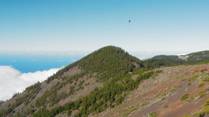 西班牙特内里费岛低密云和山峰和绿色森林上方的滑翔伞
