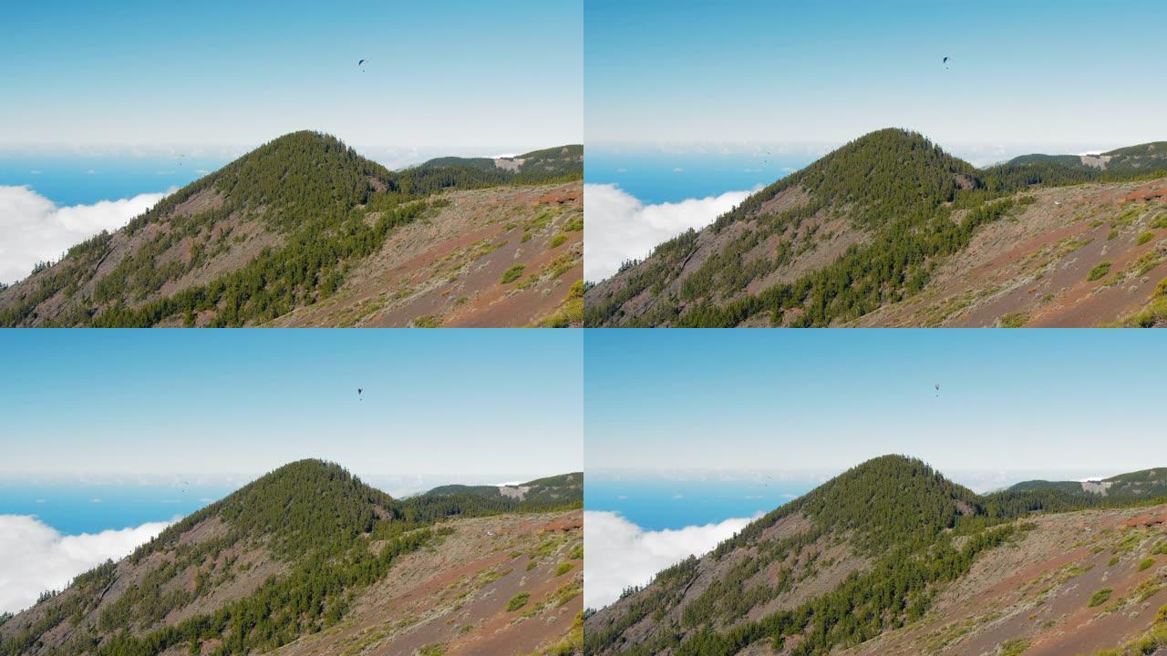 西班牙特内里费岛低密云和山峰和绿色森林上方的滑翔伞