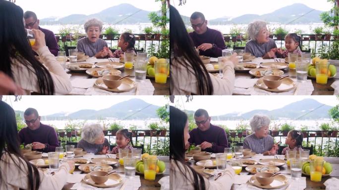 快乐的亚洲祖父母坐在后院的餐桌旁与孙女交谈