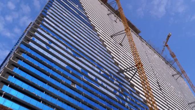 在蓝天下的建筑工地上的起重机正在建造新的摩天大楼。建筑施工
