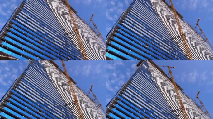 在蓝天下的建筑工地上的起重机正在建造新的摩天大楼。建筑施工