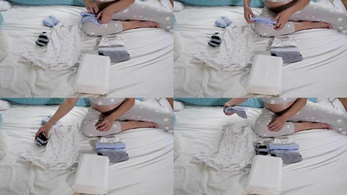 怀孕的妈妈在床上为新生儿折叠衣服