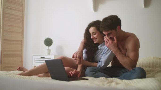 放松的情侣在家看笔记本电脑。开朗的夫妇在电脑旁大笑