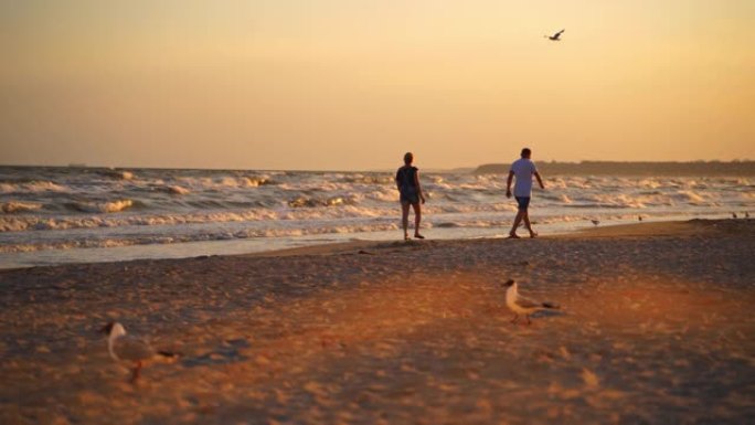 日落时走在海边的男人和女人。