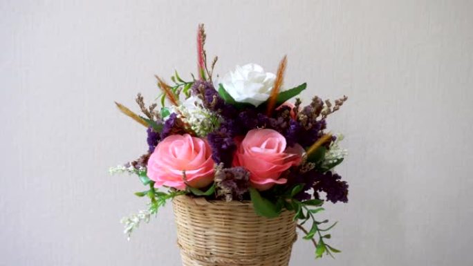 粉红色和白色的玫瑰花在编织的木制花瓶中，带有小装饰叶子，白色背景上的小花正在旋转。粉彩花卉系列展示