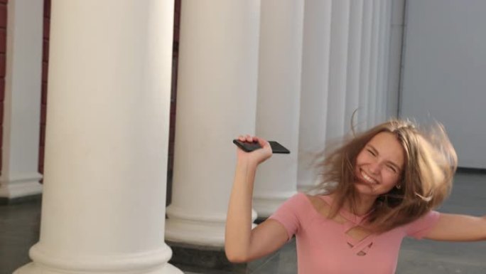 年轻的女孩拿着智能手机，穿着粉红色的高跟鞋，欢欣鼓舞，跳跃