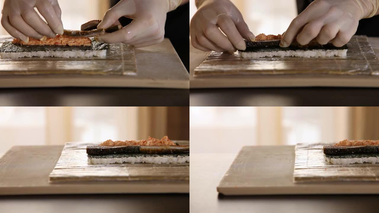 寿司厨师手的特写镜头将熏制的鳗鱼放在紫菜叶和蟹肉上。