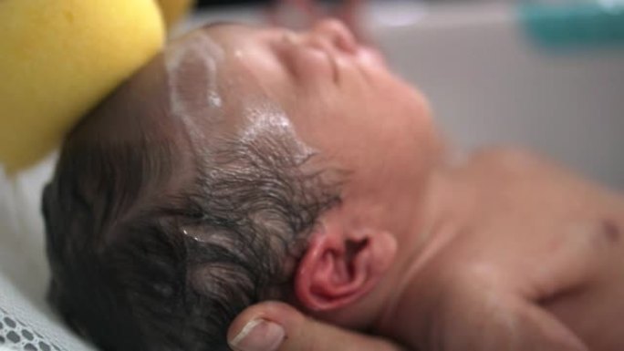 父亲和母亲的特写镜头在浴缸里洗新生男婴的头发