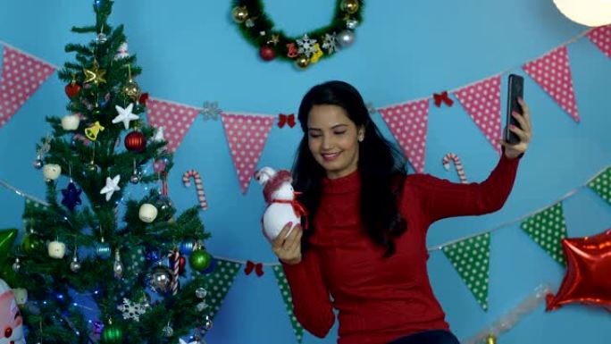 在圣诞节期间，漂亮的印度女孩用一个小玩具雪人点击自拍