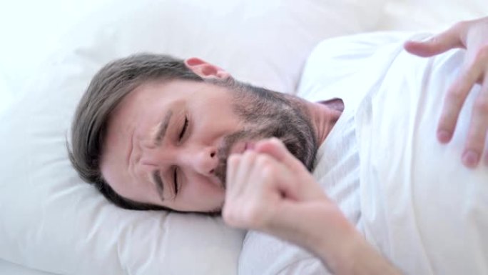 诱人的生病的年轻男性在床上咳嗽