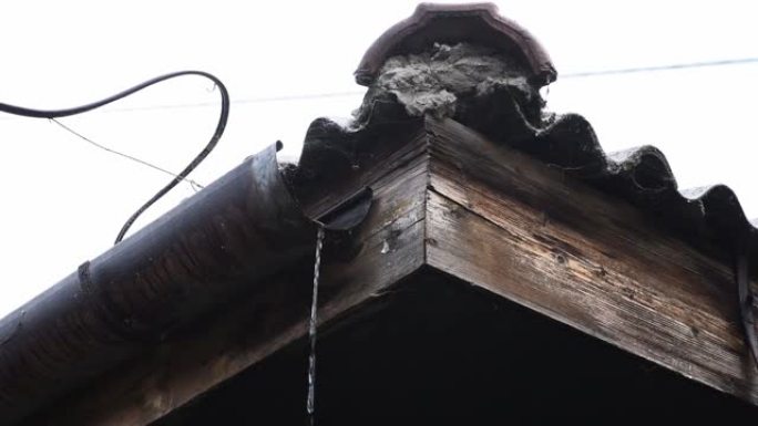 暴风雨过后，水流过房屋屋顶上破碎和损坏的旧生锈雨水槽