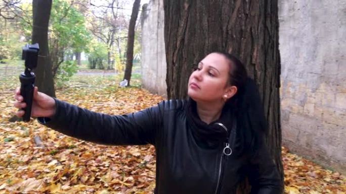 女人在秋季公园的摄录机上拍摄自己