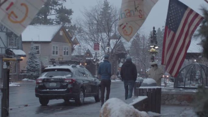 在积雪覆盖的圣诞节小镇上，一面美国国旗，人们步行和开车经过。