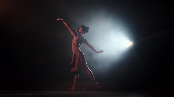 优雅的芭蕾舞演员穿着米色连衣裙，在黑暗中跳舞古典或现代芭蕾舞元素，配有泛光灯背光。黑色背景上的烟雾。
