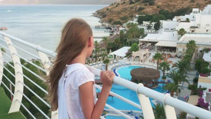 休息的女孩从游泳池和海景的室外阳台上看。旅游女孩在度假酒店游泳池附近的休息室和大堂的露台上观看。
