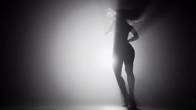 在灯光投影仪前的烟雾黑暗舞台上跳舞的女人的苗条性感剪影。艺术观念，灵活性，才华横溢的女孩。4k