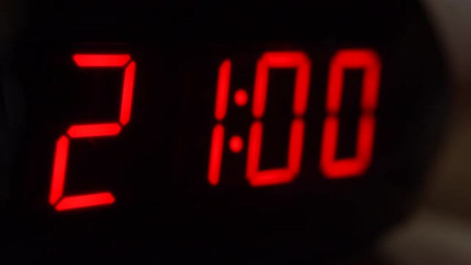 黑色数字时钟屏幕的特写显示21.00。黑色背景上闪烁红色数字。现代定时器和霓虹灯、电气设备和现代技术