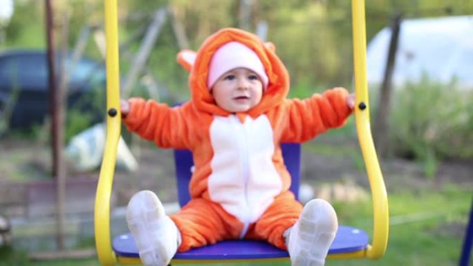 快乐的小婴儿在秋千上摇摆。这个女孩穿着cosplay fox服装。睡衣叫kigurumi。