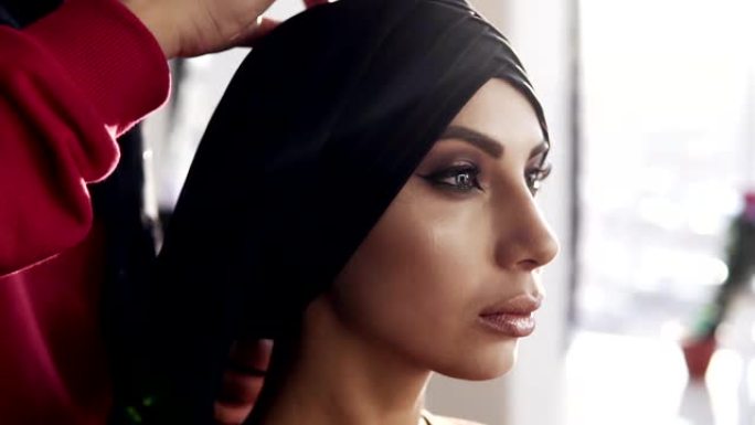美丽的女孩，传统的阿拉伯黑色头巾被背后无法辨认的女人遮住了头。专业晚装的女孩。侧视图