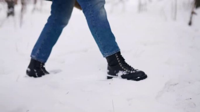 穿着黑色皮靴的女性脚在降雪时走在公园里。女人践踏雪享受圣诞节假期。下雪的冬天，女孩在森林里漫步的长角