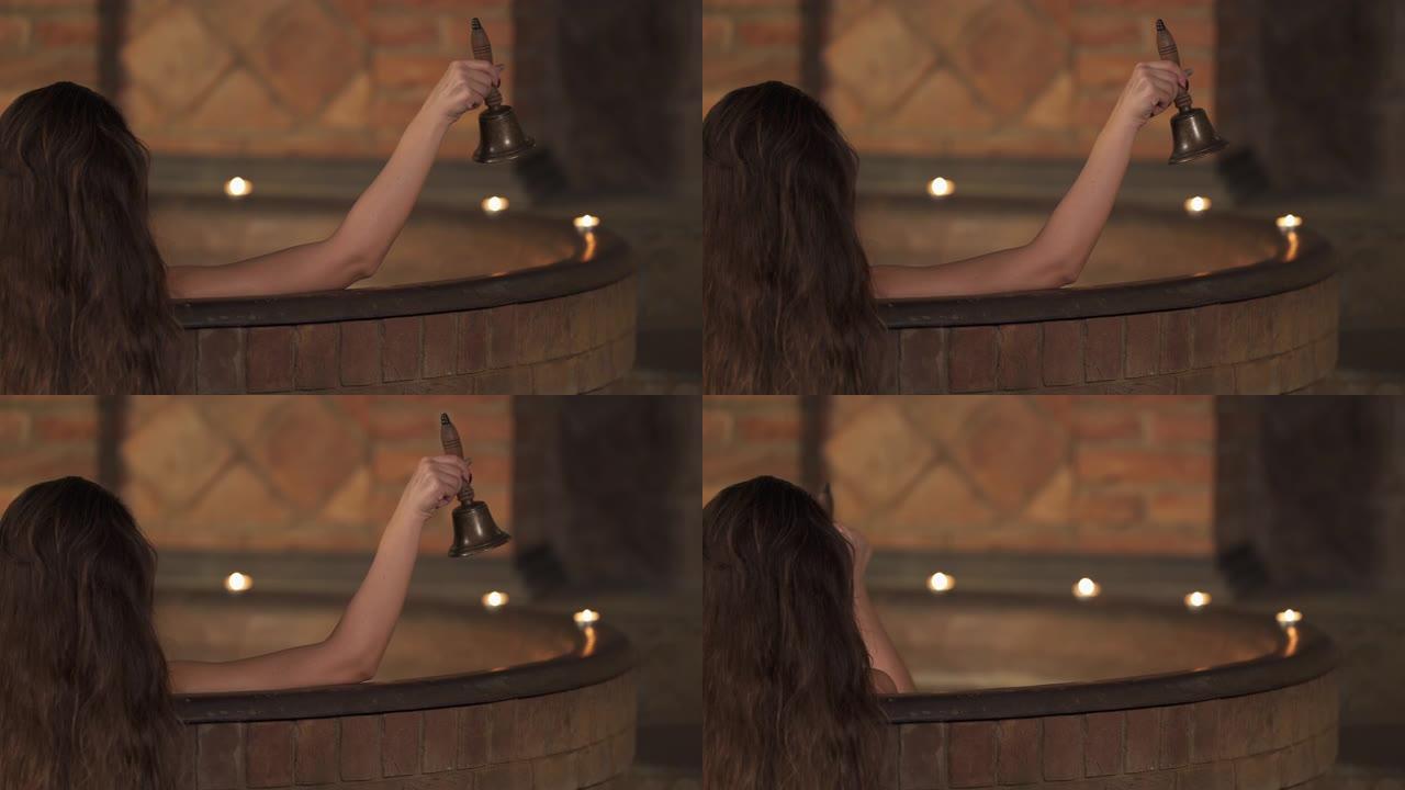 一个女人的特写镜头，有着美丽的黑发，在水疗中心洗热水澡时敲响了钟声。豪华度假概念。孤立、模糊的背景