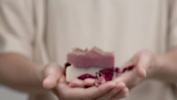 女人的手拿着一块玫瑰肥皂。特写模糊; 当她向前移动双手时，情况变得清晰。