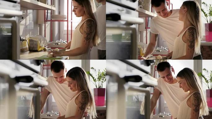 这位漂亮的欧洲年轻女子正在阳光明媚的厨房里和她英俊的高挑微笑的丈夫一起做饭