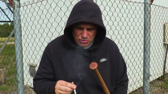 一个拿着棒球棒在篱笆附近抽烟的人
