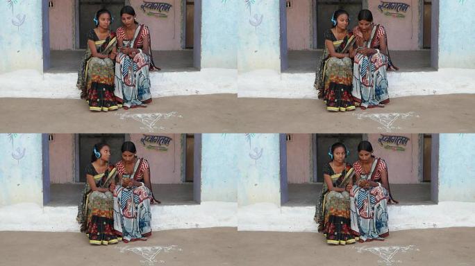 两名妇女在印度拉贾斯坦邦农村的家中戴着耳机听音乐，穿着传统服装，色彩鲜艳，印花艺术设计，当地工艺纱丽