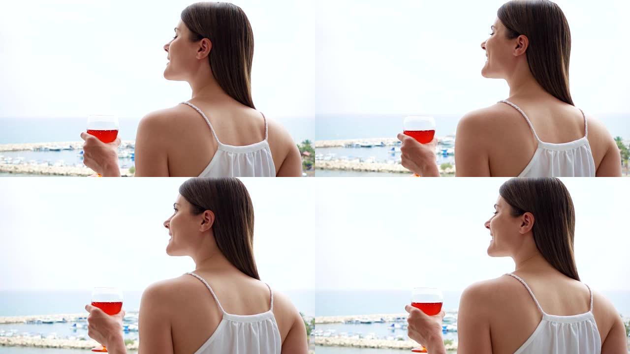 女人从露台上欣赏海景。度假女性在阳台上慢动作喝玫瑰酒